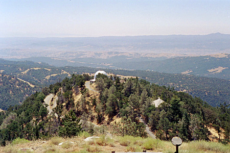 [The dome is mostly hidden behind some tree. The valley below is expansive and includes many trees at all levels. There are some narrow openings winding through the trees which is probably the roadway to the top since there are no other buildings on the mountain.]